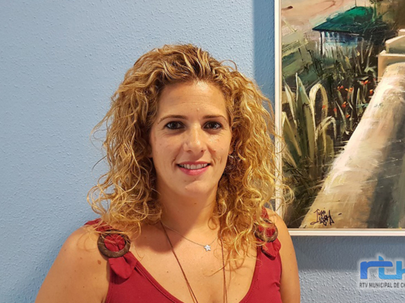 Mujer sonriente en una exposición de arte, con un lienzo de paisaje al fondo.