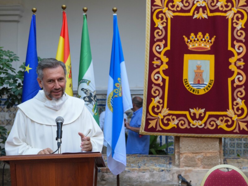Una persona hablando en un podium con banderas de España y Andalucía al fondo.