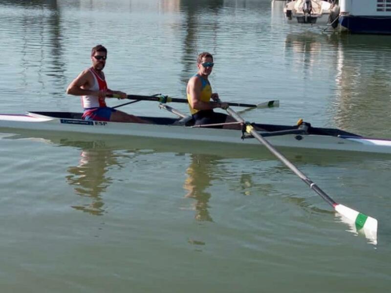 Dos atletas remando en una canoa doble en un entorno acuático tranquilo.