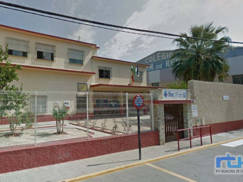 Colegio Municipal de Chipiona, ubicado en la calle Mayor, con un edificio principal y un jardín infantil al frente, rodeado de una cerca metálica y con un árbol de palma en el lado derecho.