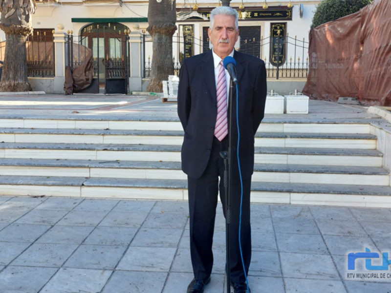 Hombre en traje hablando en un micrófono en una plaza con escaleras y edificios en el fondo.