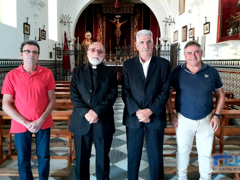 Cuatro personas posan juntas en una iglesia, rodeadas de bancos y decoración religiosa.