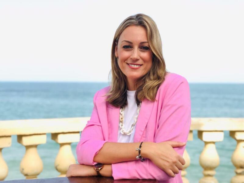 Elegante mujer con chaqueta rosa frente al mar.