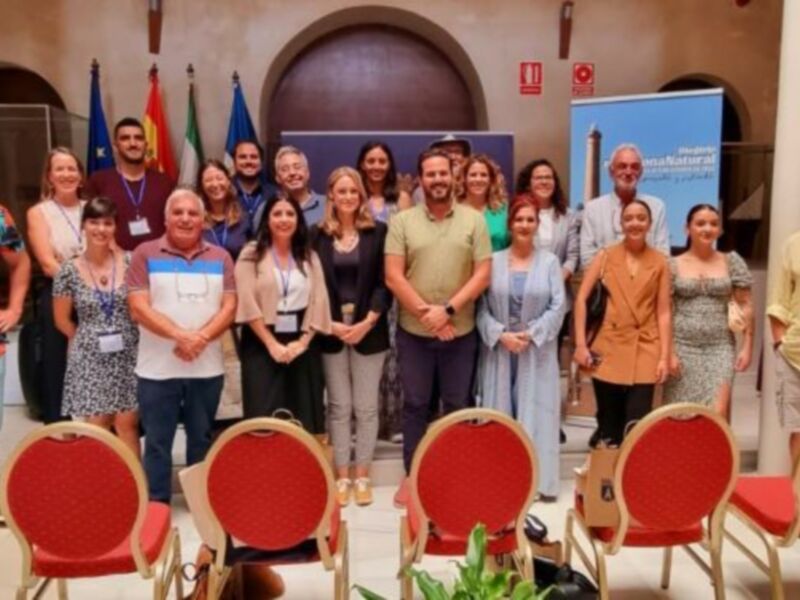 Grupo de personas posando para una foto en un evento formal, con banderas de diferentes países en el fondo.