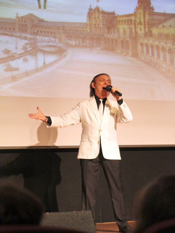 Cantante en escenario con Plaza de España en fondo proyectado.