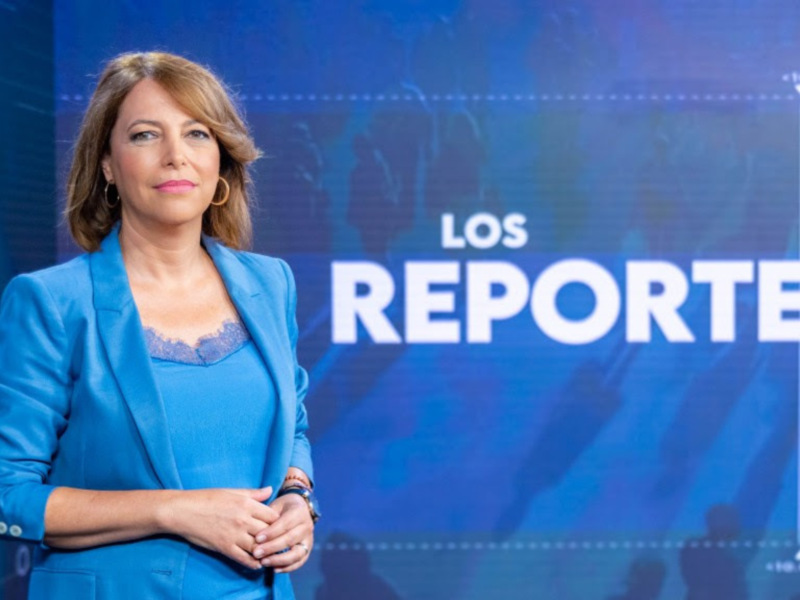 Mujer en traje azul frente a fondo azul con letras blancas que dicen 'LOS REPORTEROS'.
