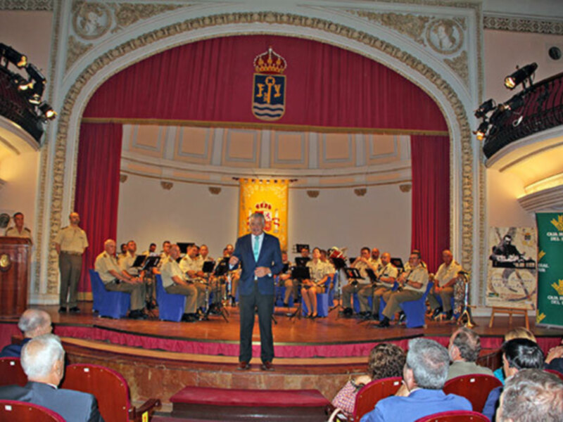 Concierto de banda en un teatro con escenario decorado y público asistiendo.