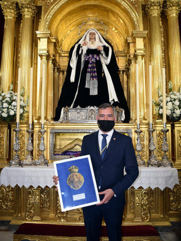 Un hombre en traje sostiene un retrato enmarcado en un altar dorado con una imagen de la Virgen María.