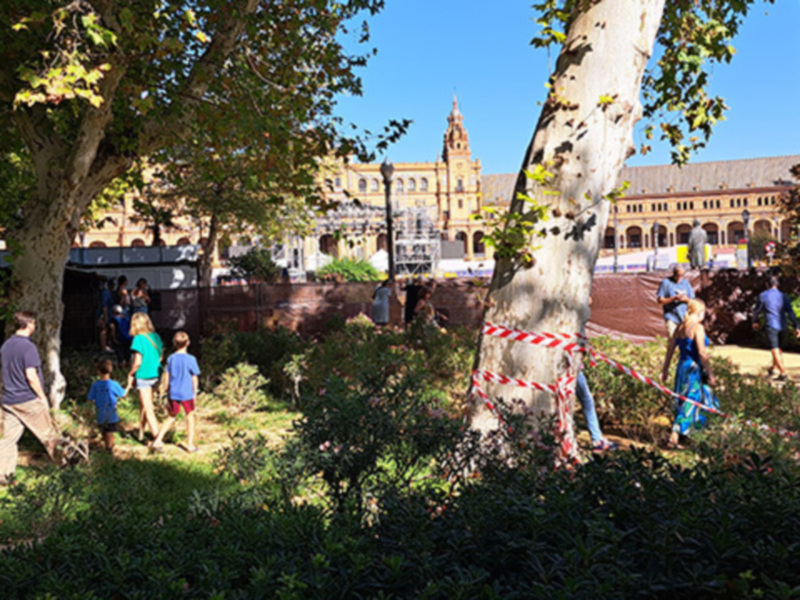 Árboles y jardín con edificio histórico al fondo en un día soleado.