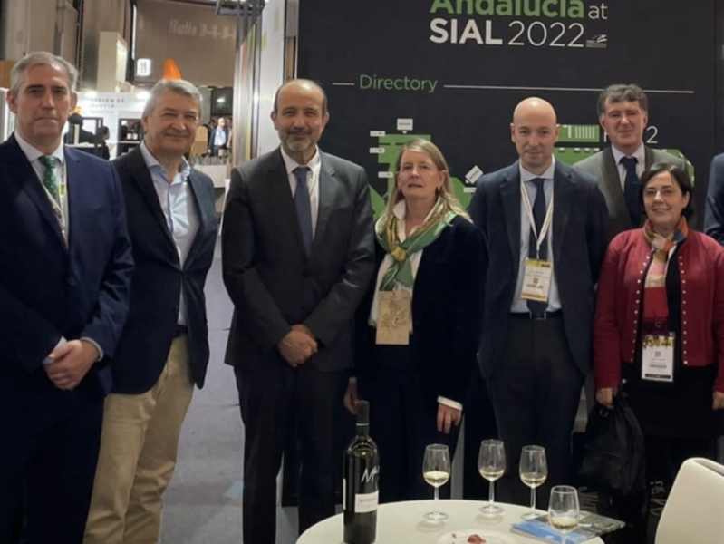 Una reunión formal en el stand de Andalucía en SIAL 2022, con personas en trajes y una botella de vino en el centro de la mesa.