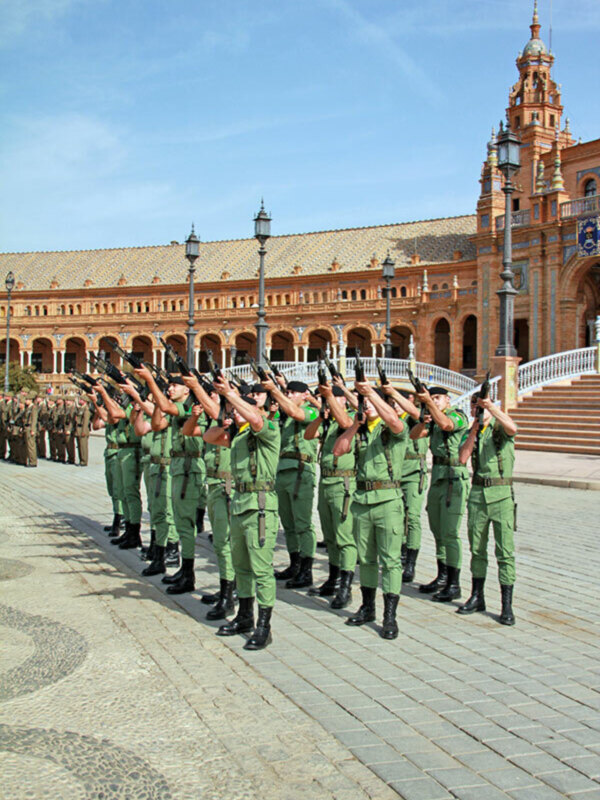 Desfile militar en Plaza de España, Sevilla, España, con soldados en formación y uniformes verdes.