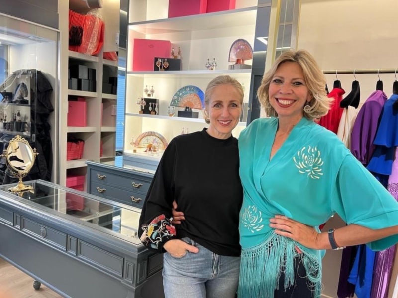 Dos mujeres sonríen en una tienda de moda, rodeadas de ropa y accesorios.
