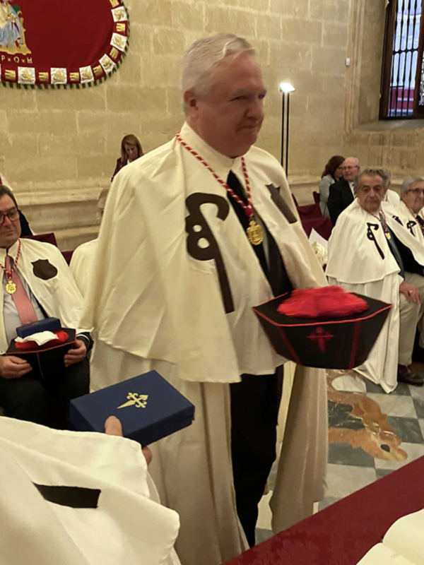 Un hombre en traje blanco con insignias y una corona en la cabeza, posiblemente en un evento formal o religioso.