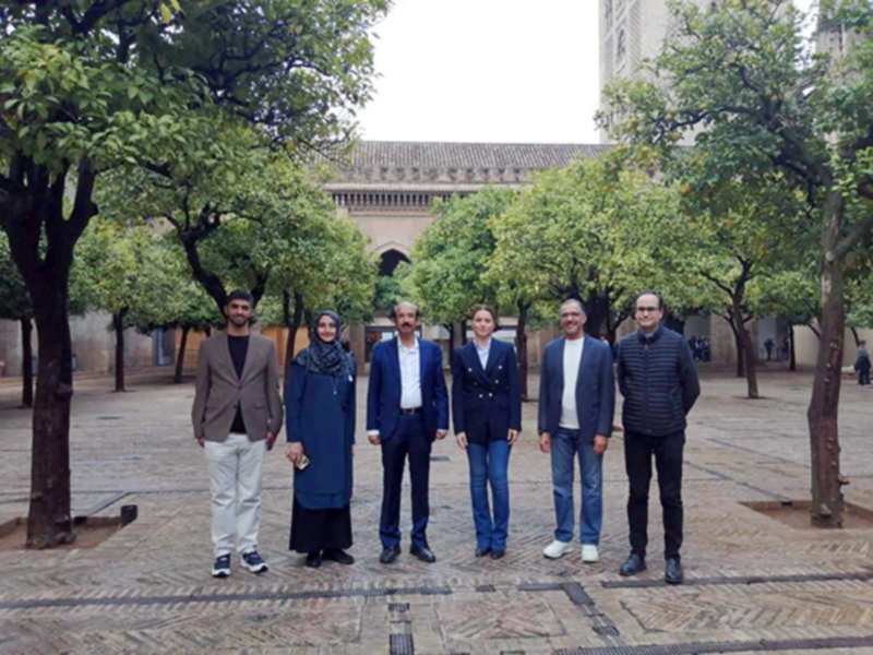 Una escena en un patio con árboles y una torre en el fondo, donde seis personas posan juntas. La imagen parece ser de una reunión o evento formal en un entorno histórico o educativo.