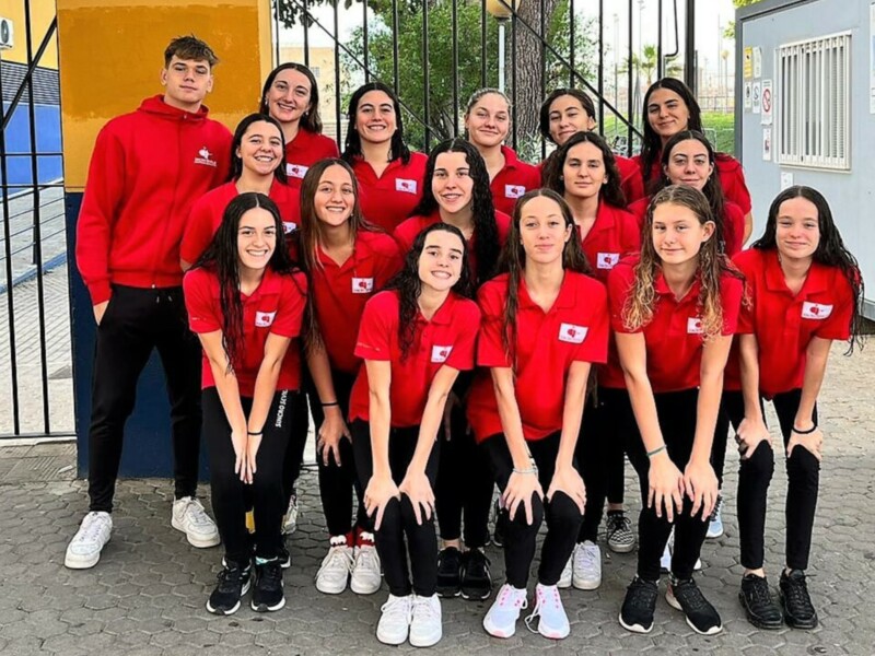 Equipo deportivo femenino en uniforme rojo, posando juntos en un entorno urbano.