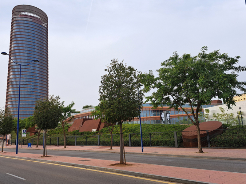 Edificio de oficinas moderno junto a un parque urbano con árboles y sendero peatonal.