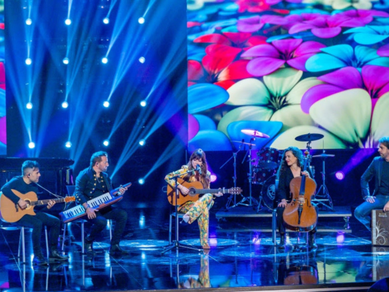 Grupo musical en escenario con luces azules y fondo de flores multicolores.