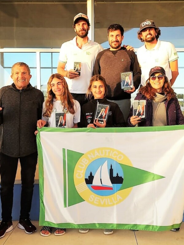 Equipo ganador del torneo de vela del Club Náutico de Sevilla con trofeos y bandera del club.