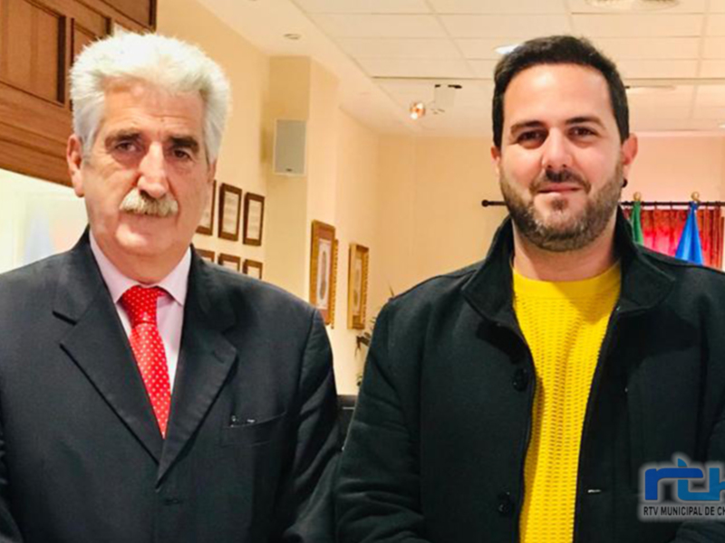Dos personas posando para una foto en una oficina con decoración oficial.