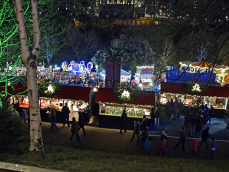 Una feria nocturna con stands iluminados y gente caminando en un parque.