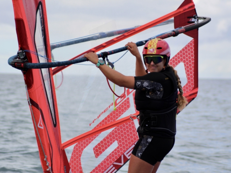 Una persona disfruta de la windsurfing en el mar, con un casco y gafas de protección para seguridad.