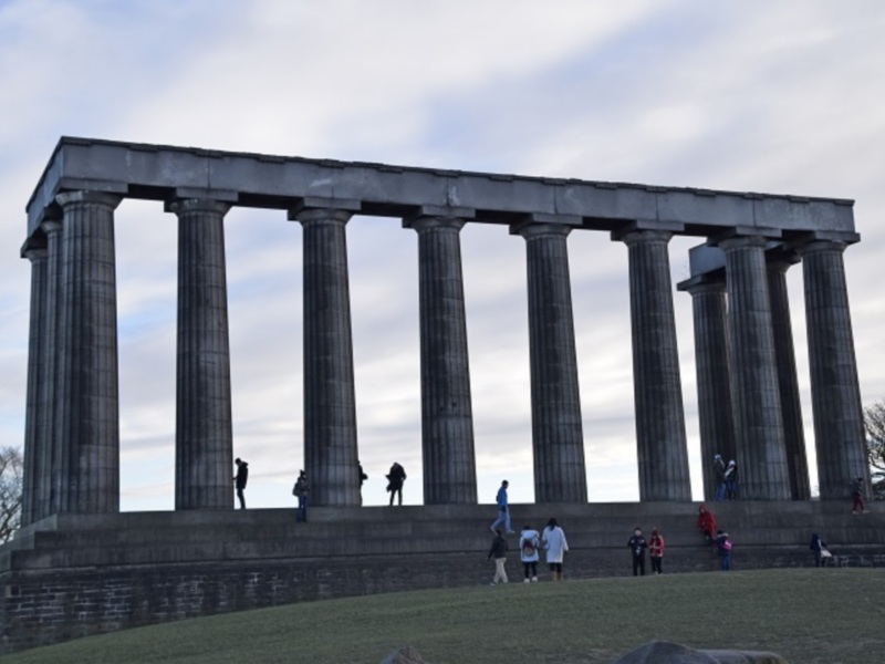 Una vista de un monumento con columnas y personas en el fondo, iluminado por un cielo nublado.