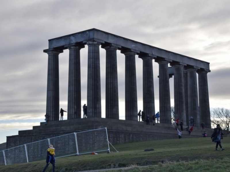 Monumento Nacional de Escocia en Edimburgo, con visitantes y un campo de fútbol en el primer plano.