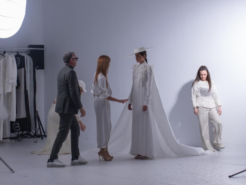 Tras la escena de un ensayo fotográfico con modelos en ropa blanca y accesorios, bajo iluminación profesional.