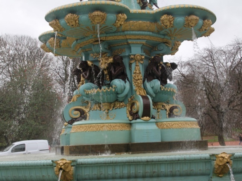 Fountain with ornate golden details and water jets in a park setting.