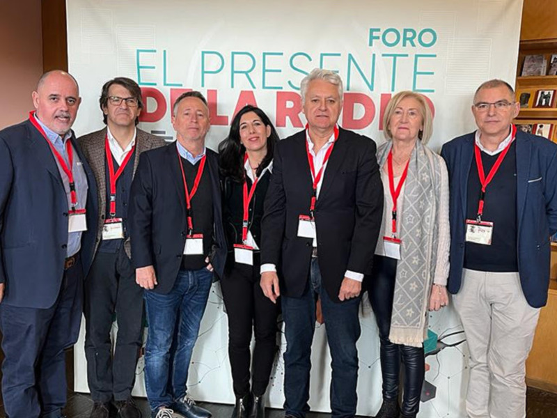 Grupo de personas posando frente a un cartel con el texto 'EL PRESENTE' en un evento o conferencia.