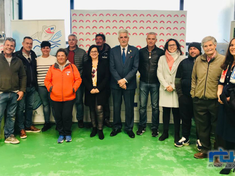 Gente posando para una foto en un evento empresarial, con un fondo de pared con patrones de colores y una persona con una chaqueta de lana blanca y negra.