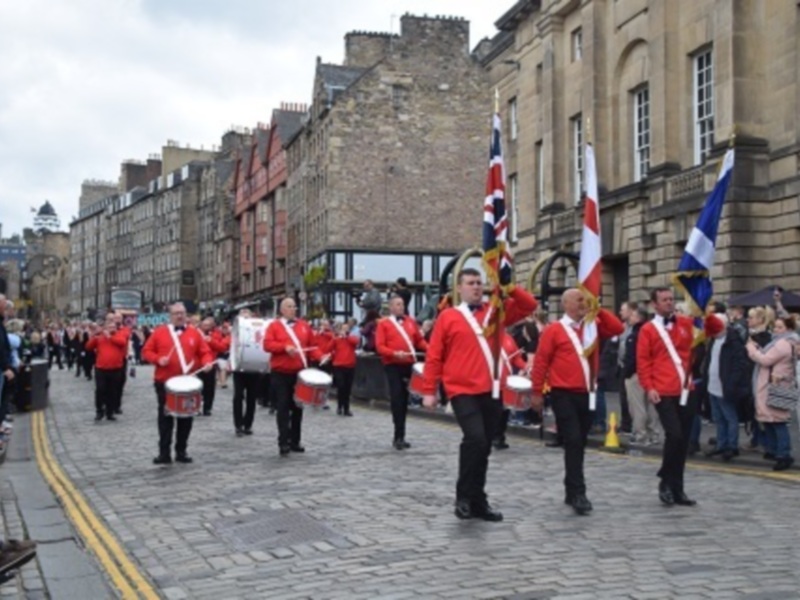 Desfile militar en Edimburgo, con soldados en uniforme rojo y banderas británicas y escocesas ondeando.