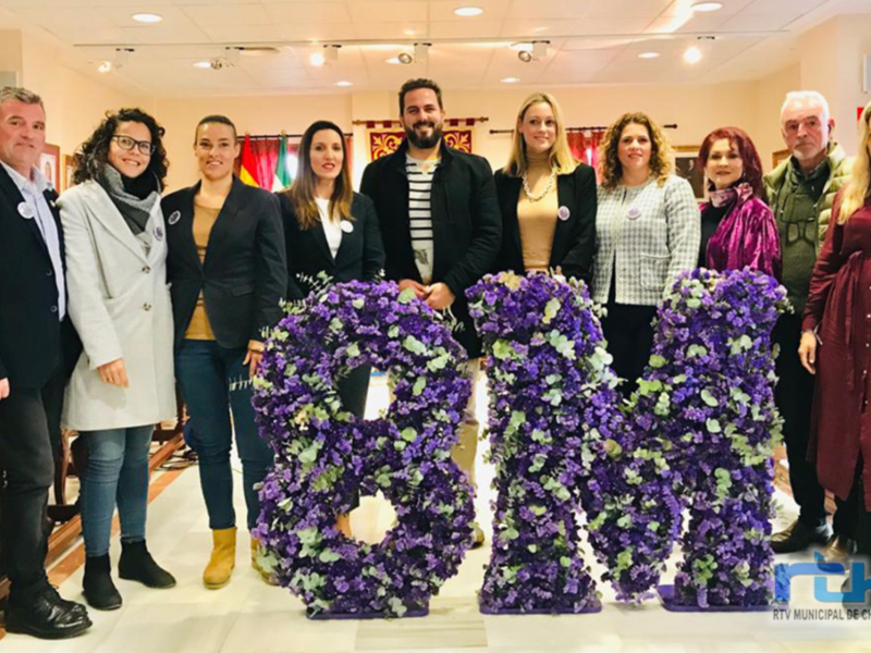 Grup de persones en una reunió oficial davant unes guirlandes de flors viola.