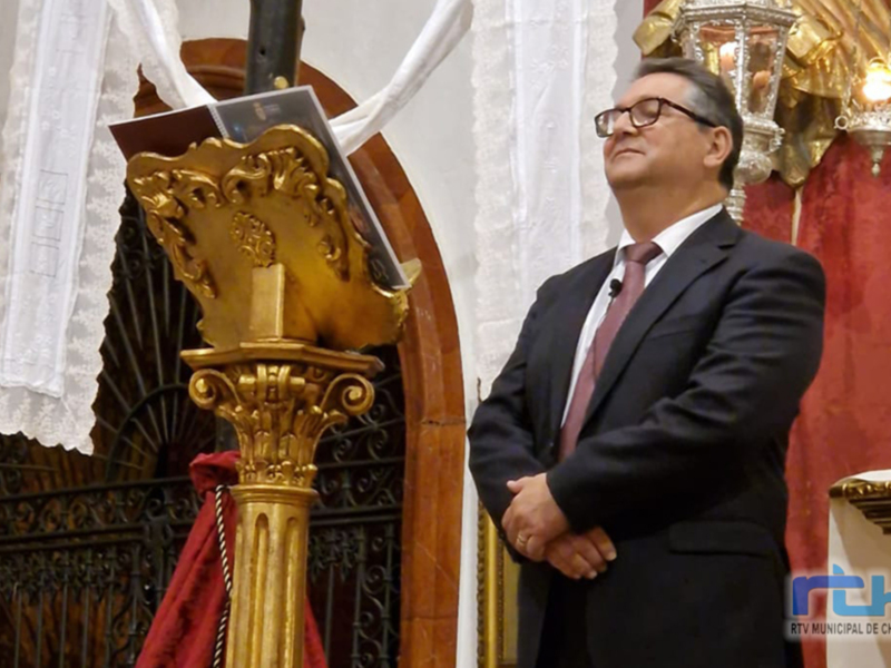 Persona en traje y corbata en un entorno religioso, posiblemente durante una ceremonia o homilía.