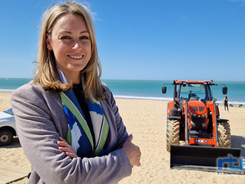 Reportera en la playa con maquinaria de construcción en el fondo.
