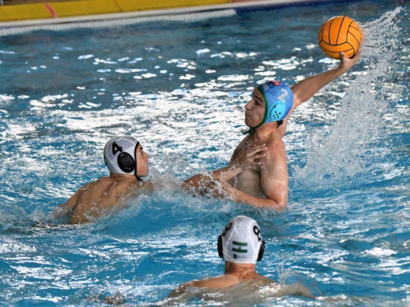 Jugadores de polo aquático en acción en una piscina, con el balón en movimiento.