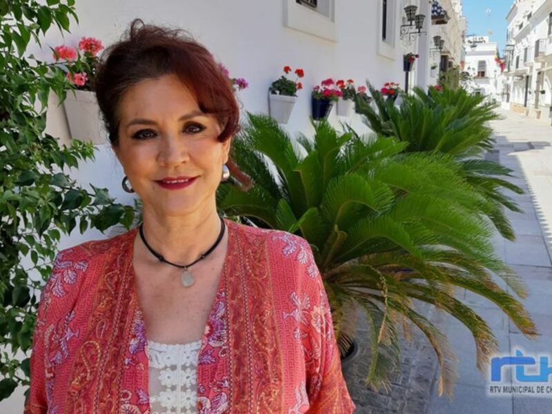 Una mujer con vestido rojo y cabello rojo en una calle con plantas y flores.