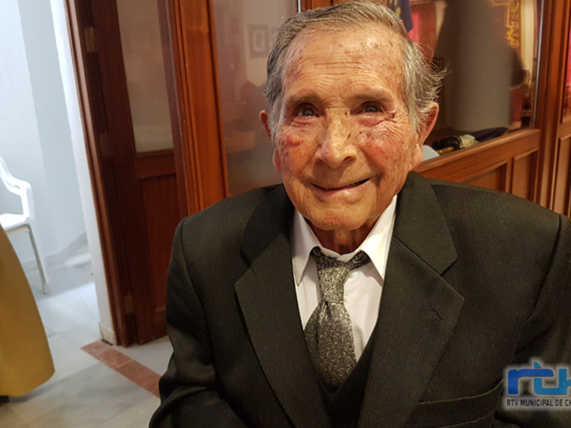 Retrato de un anciano vestido formalmente en un ambiente interno.