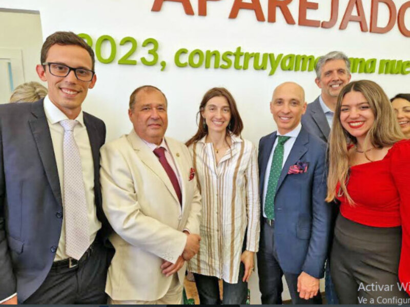 Grupo de personas sonrientes posando juntos en un evento de 2023, con el lema 'construyamos una nueva era' en el fondo.