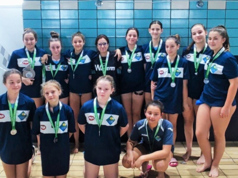 Equipo de natación femenino con medallas, posando en una piscina.
