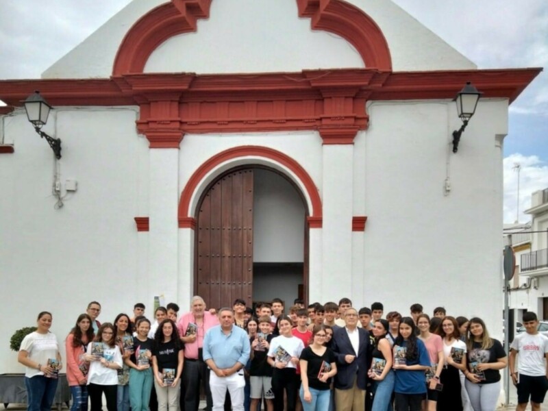 Grupal frente a una iglesia blanca con detalles rojos, posiblemente un evento cultural o educativo.