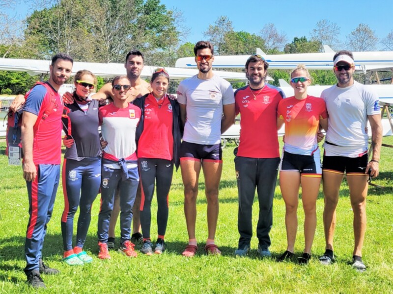 Equipo de remo posando con sus barcas en un día soleado.