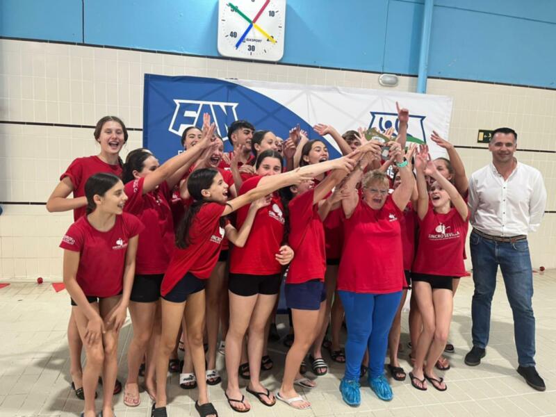 Equipo de natación celebrando un triunfo con el trofeo en una piscina.