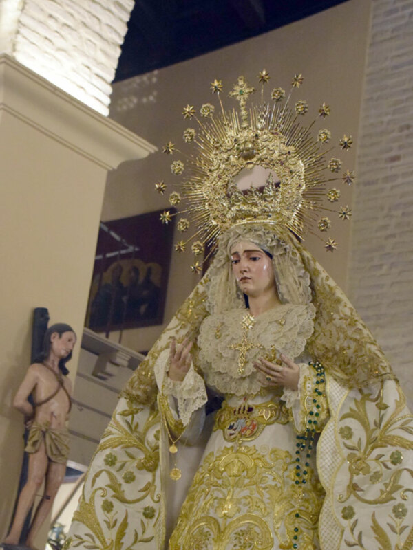 Imponente imagen de la Virgen María en traje dorado y corona ornada, en un entorno religioso.