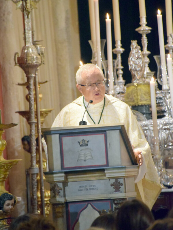 Un sacerdote pronuncia un sermón durante una ceremonia religiosa en una iglesia decorada con velas y ornamentos dorados.