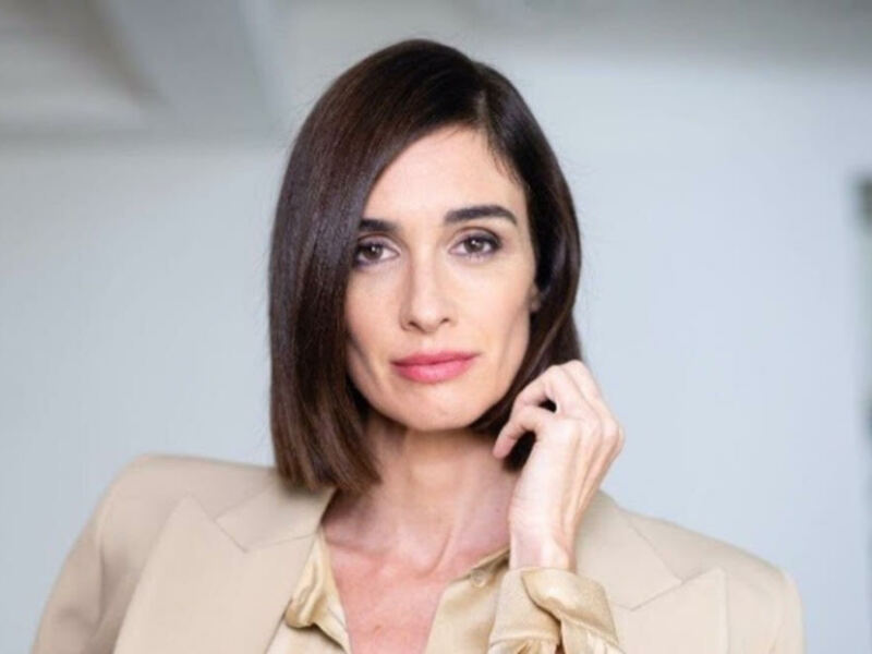 Elegante mujer con cabello largo y liso, vistiendo un traje beige en un entorno minimalista.