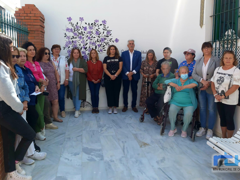 Grupal de personas posando frente a un mural floral en un patio urbano.