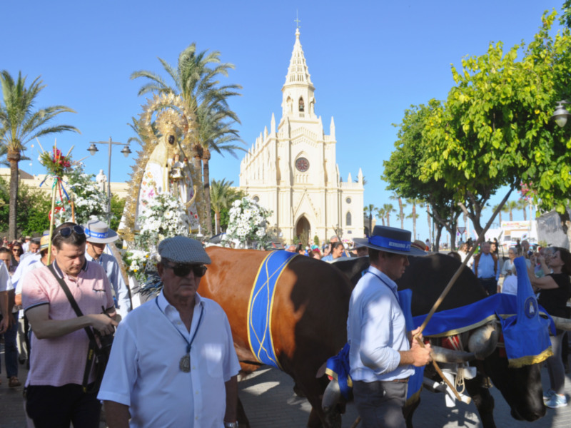 Desfile religioso con una imagen de la Virgen y un toro en el centro, con una iglesia en el fondo y personas observando la procesión.