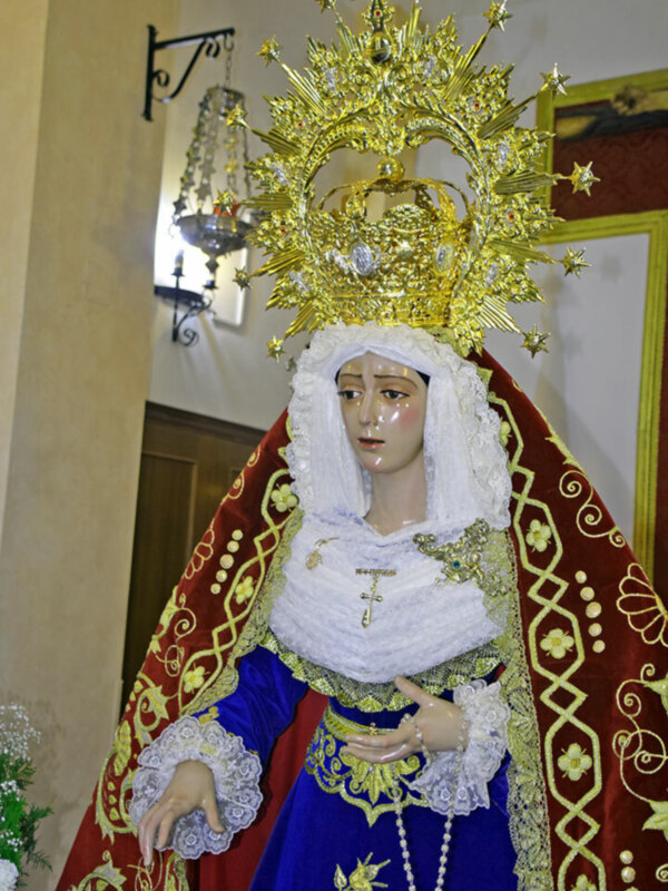 Figura religiosa con vestimenta y corona dorada en un entorno interior.