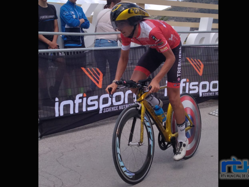 Ciclista en competición durante una etapa de la carrera, con uniforme rojo y negro y casco amarillo. Fondo con publicidad de 'InfiSport' y público en el estadio.
